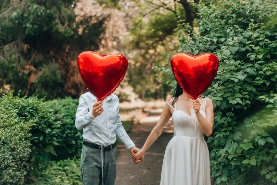 גבר ואישה מחזיקים ידים ומסתירים את פניהם עם בלונים אדומים